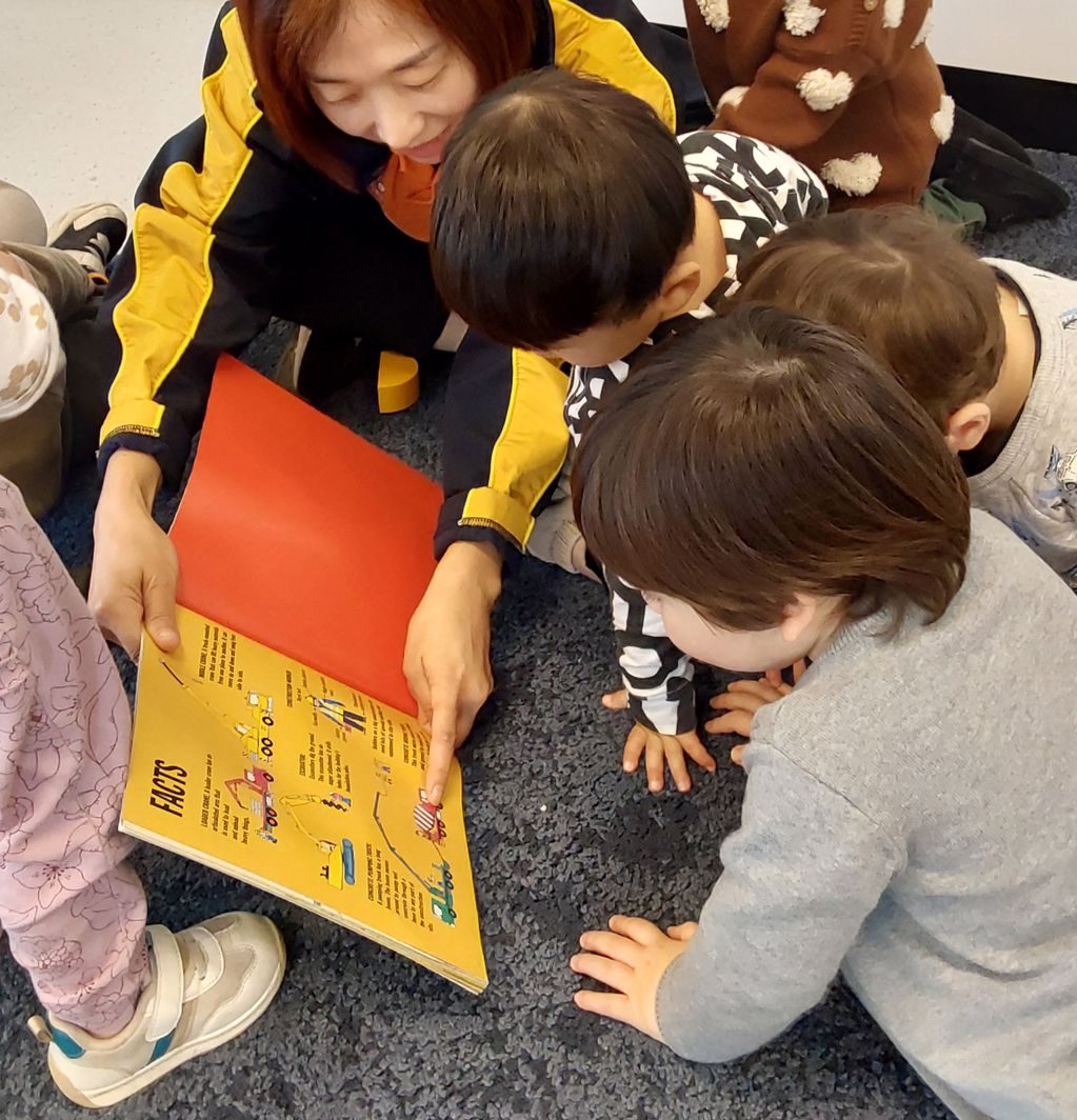 Early learning teacher reading a storybook to a group of engaged children in a classroom.