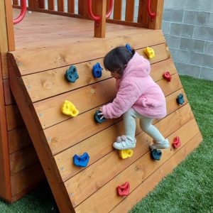 Toddler climbing a wall climbing board in a kids' play area for early learning and motor skill development.